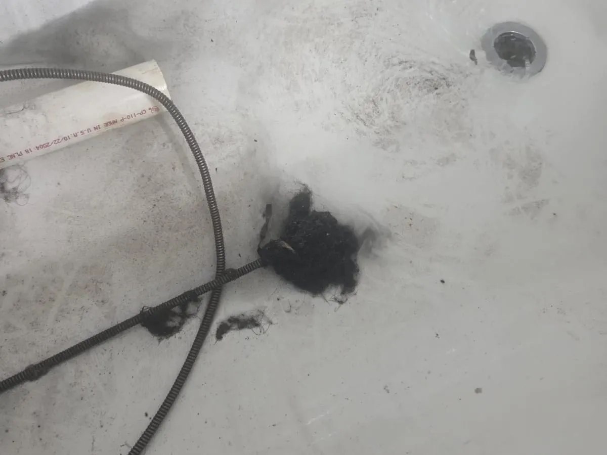 A drain cable lying in a white bathtub beside the drain, next to a clump of dark debris pulled out of the line