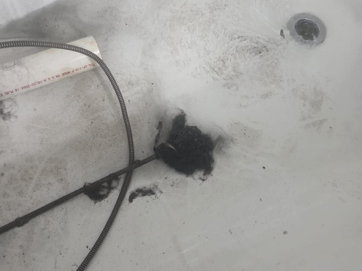 A drain cable lying in a white bathtub beside the drain, next to a clump of dark debris pulled out of the line