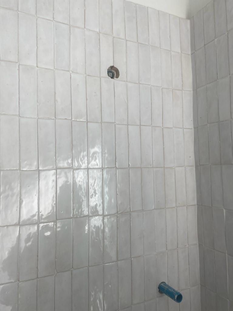 A shower wall in glossy white stacked tile, with a capped shower arm stub near the top and a tub spout stub near the floor